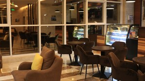 A modern indoor seating area with multiple tables and chairs, large windows, and a view of a food display. - Pearl Of Vision Hotel (Jeddah)