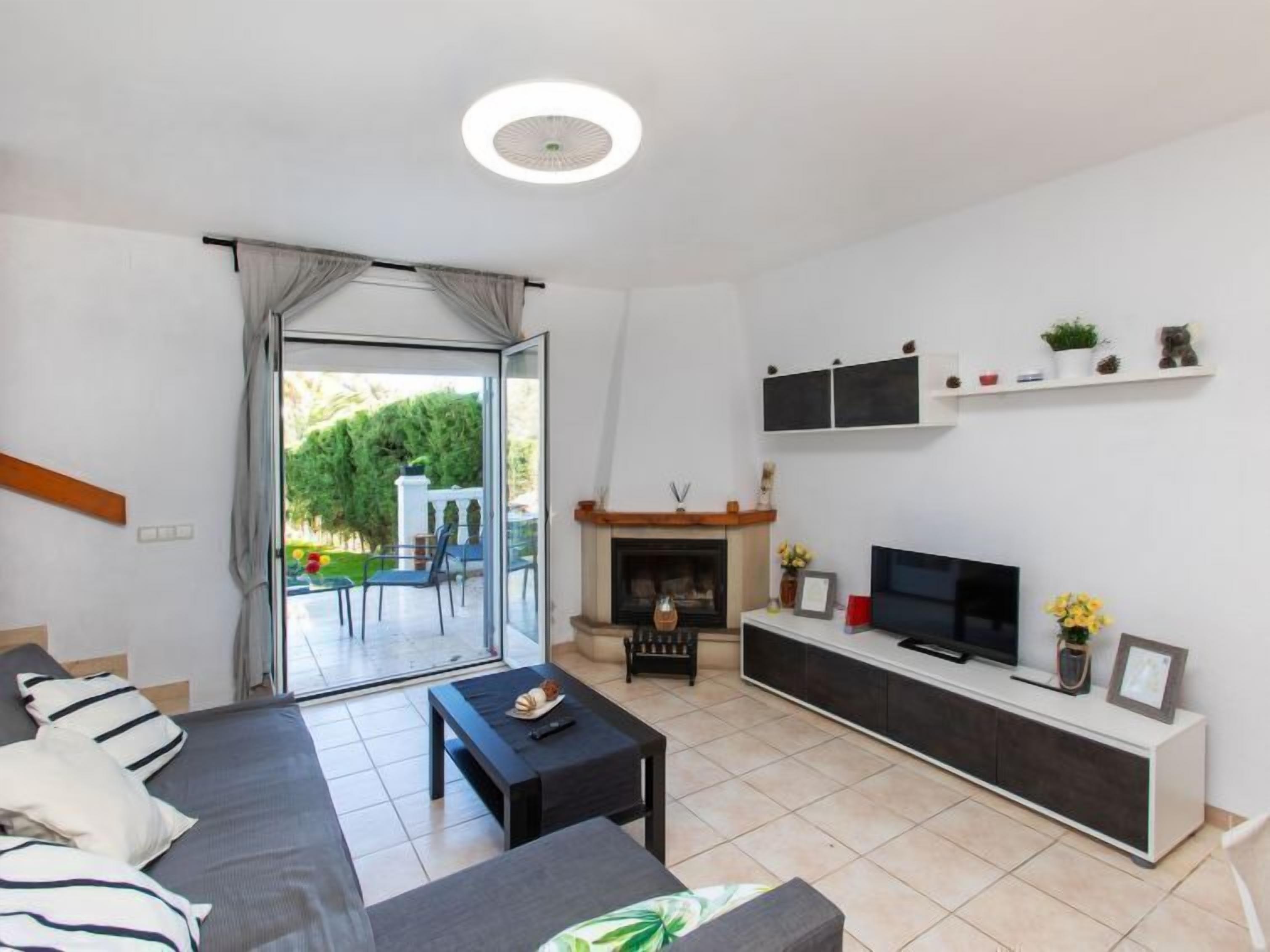 Uma sala de estar moderna com sofá, mesa de centro, televisão, lareira e uma varanda com mobiliário de exterior.