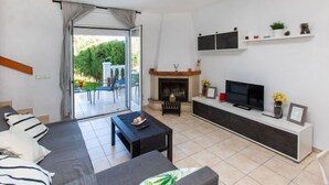 A modern living room with a sofa, coffee table, TV, fireplace, and a balcony with outdoor furniture. - Villa Zefir by Interhome (Miami Platja)