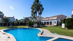 A swimming pool with a stone border, surrounded by a well-maintained lawn and palm trees. - Villa Zefir by Interhome (Miami Platja)