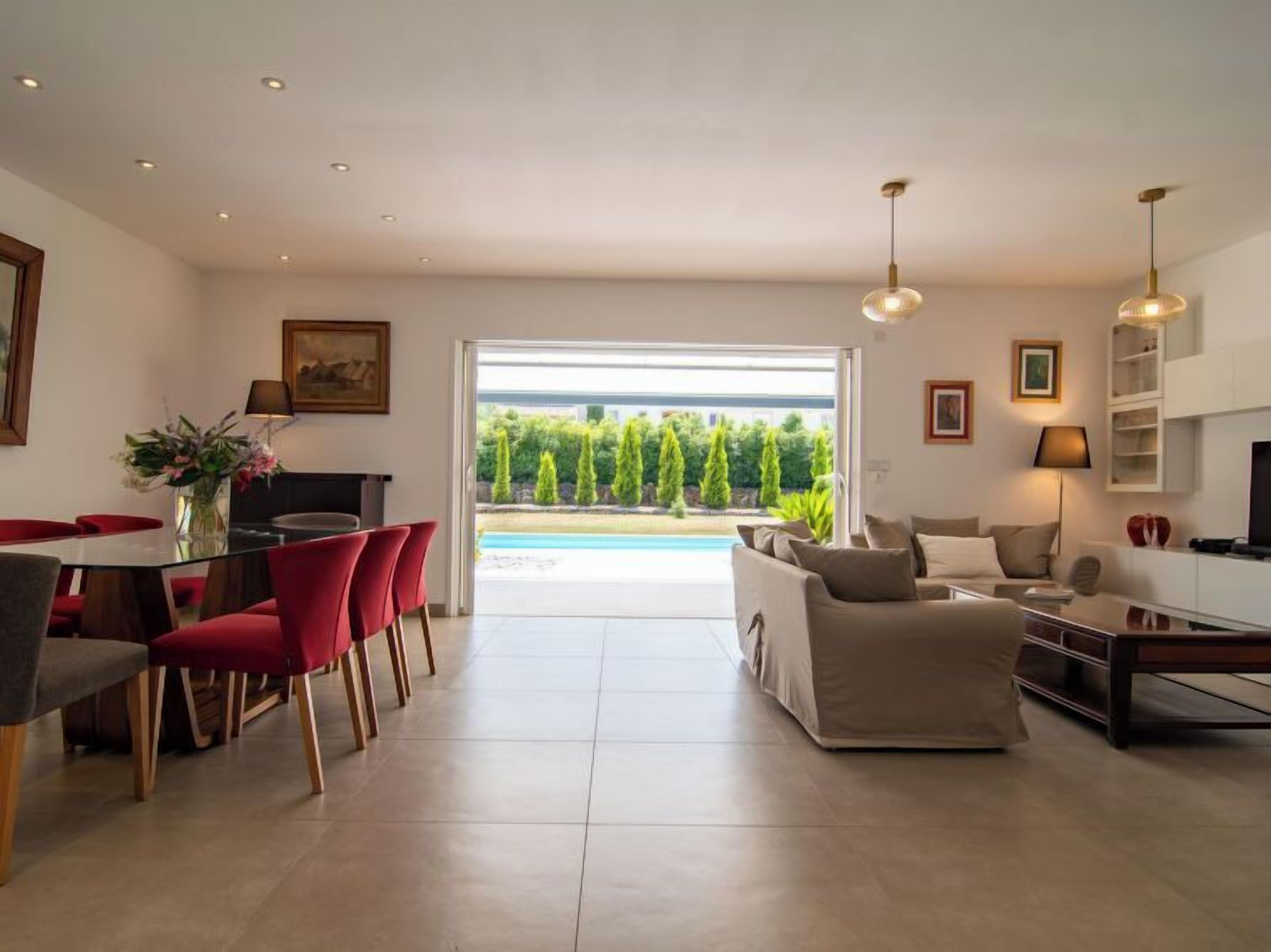 Een moderne woonkamer met een bank, een eethoek met rode stoelen en een keuken.