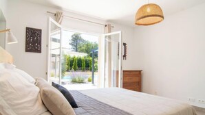 A bedroom with a bed, a wooden dresser, and a view of a garden through an open door. - Villa D'Allongue by Interhome (Callian)