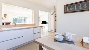 A modern kitchen with white cabinetry, a large window, and a dining area with bowls and cups. - Villa D'Allongue by Interhome (Callian)