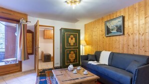 Ein gemütliches Wohnzimmer mit einem blauen Sofa, einem Holzschrank mit Kunstwerken, einem kleinen Tisch mit Tassen und einem gemusterten Teppich.