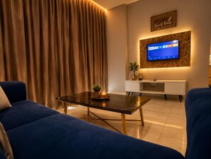 A modern living room with a sofa, a coffee table, a TV mounted on the wall, and a decorative sign above the TV. - Stirling Suites (Miri)