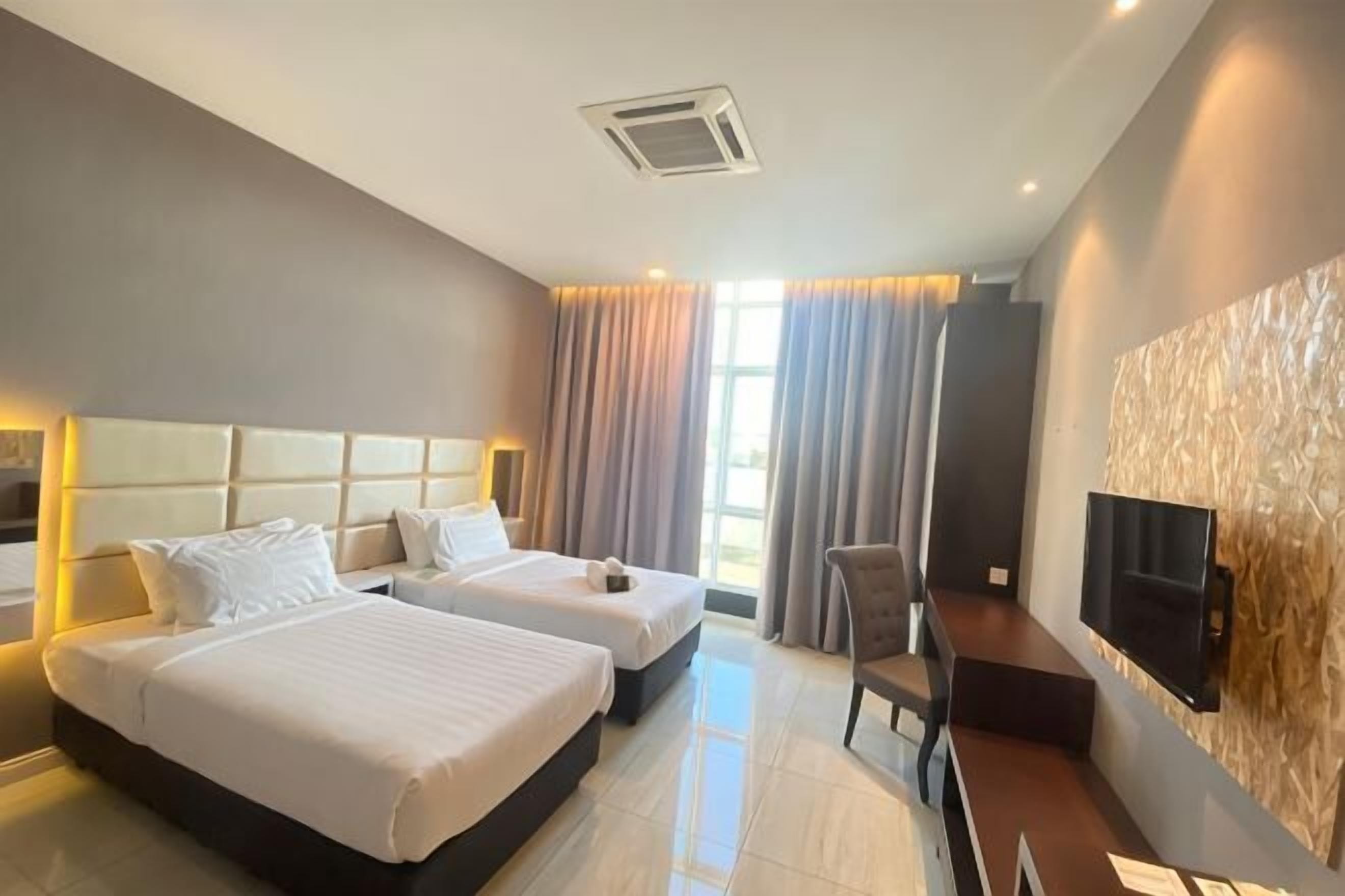 A hotel room with two beds, a TV, and a desk.