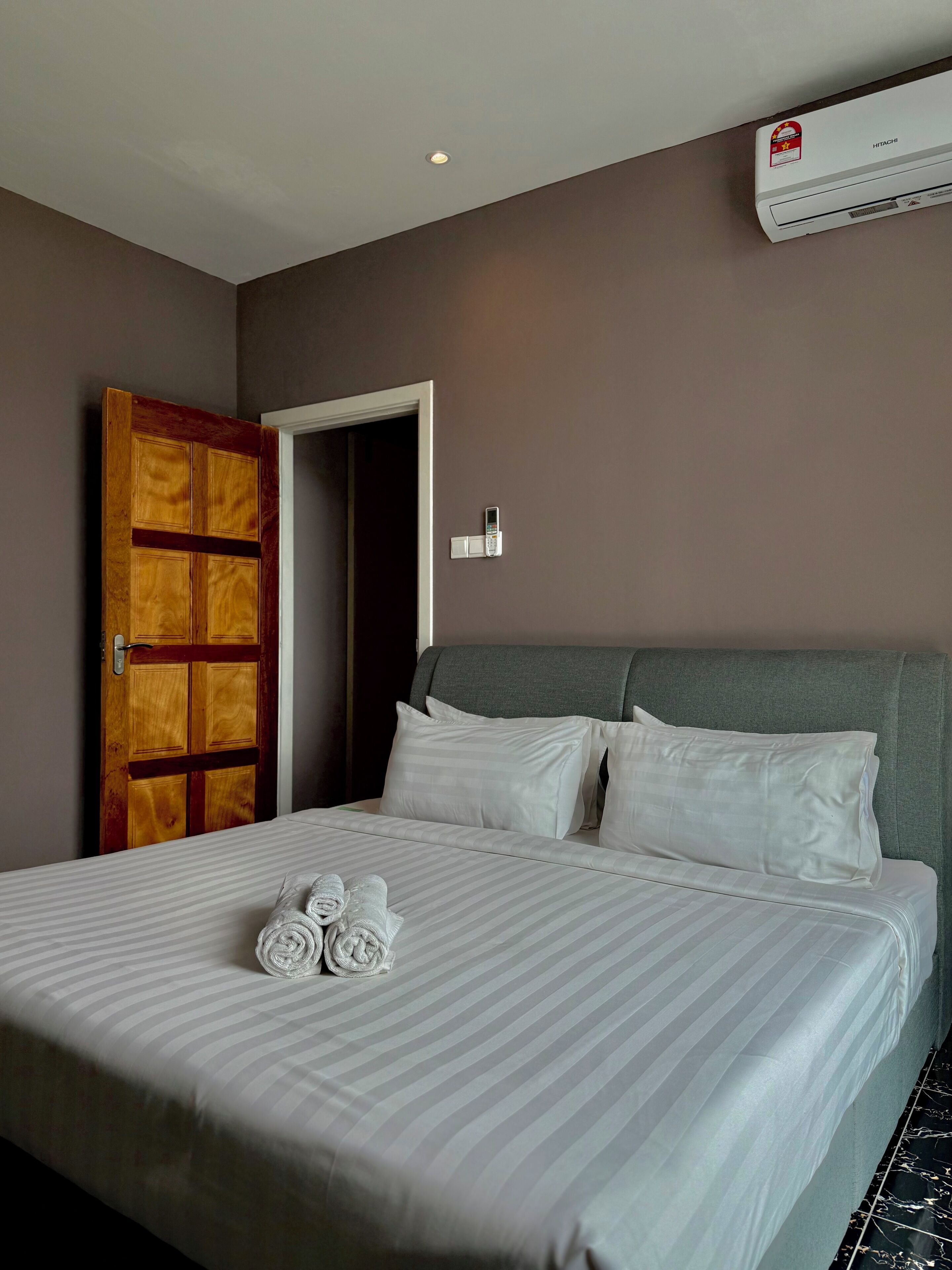 A hotel room with a bed, a wooden door, an air conditioning unit, and a phone on the wall.