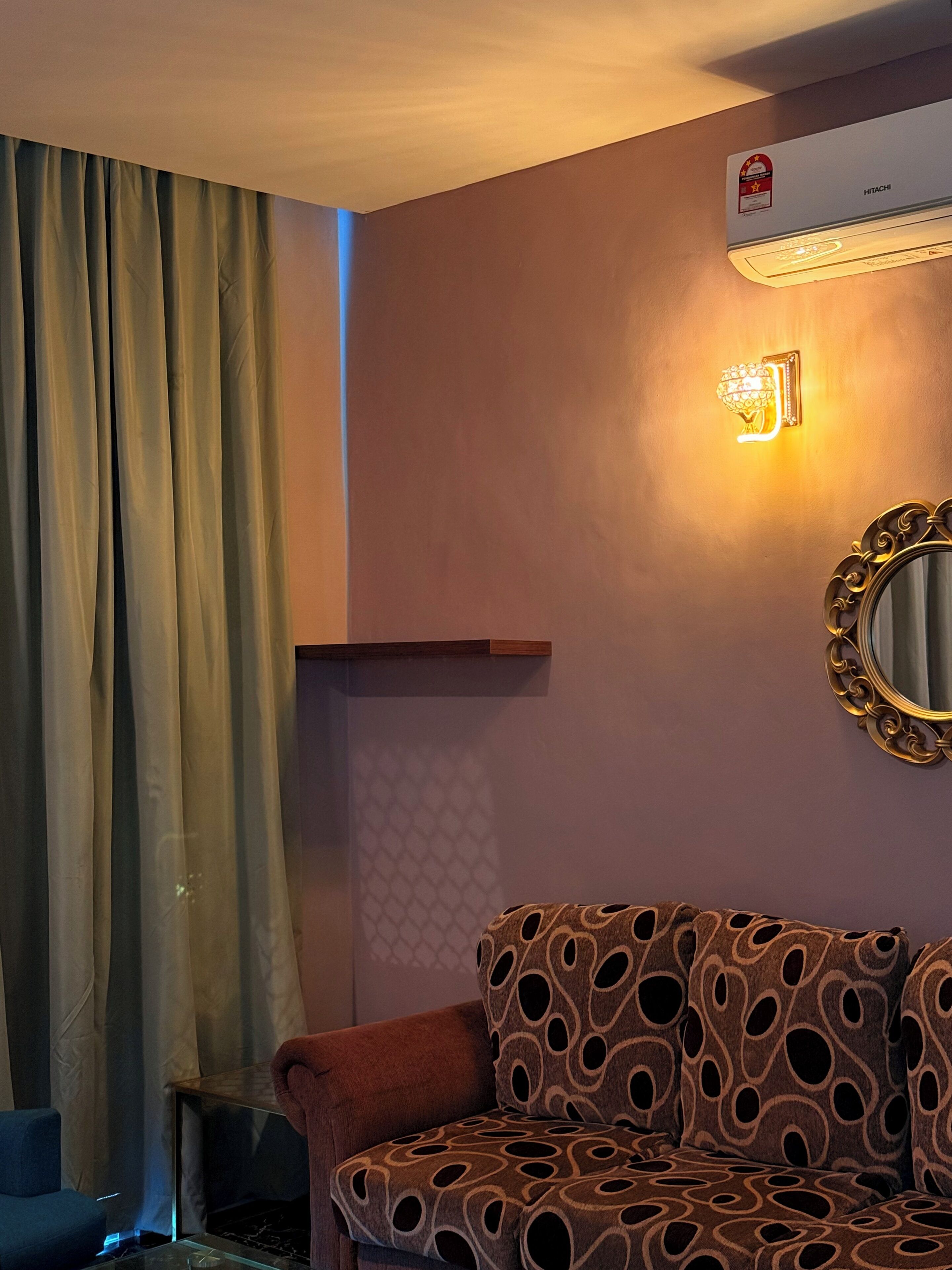 A room with a patterned sofa, a wall-mounted air conditioner, a decorative light fixture, and a window with curtains.