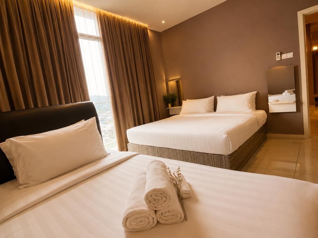 Quarto de hotel com duas camas, uma janela grande com cortinas, mesa de cabeceira com abajur e um espelho.