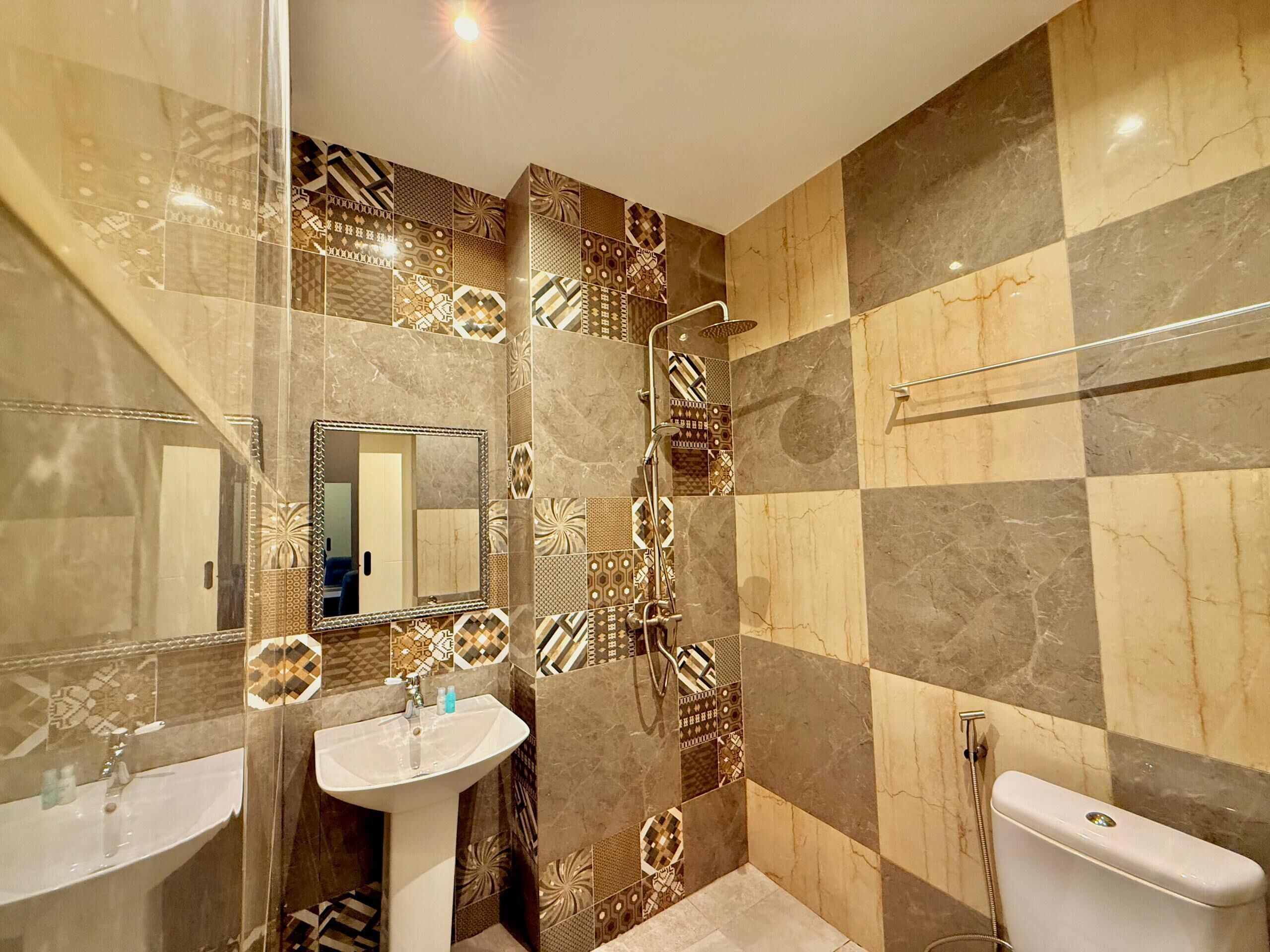Een badkamer met een betegelde muur in ruitpatroon, een wastafel, een spiegel en een toilet.