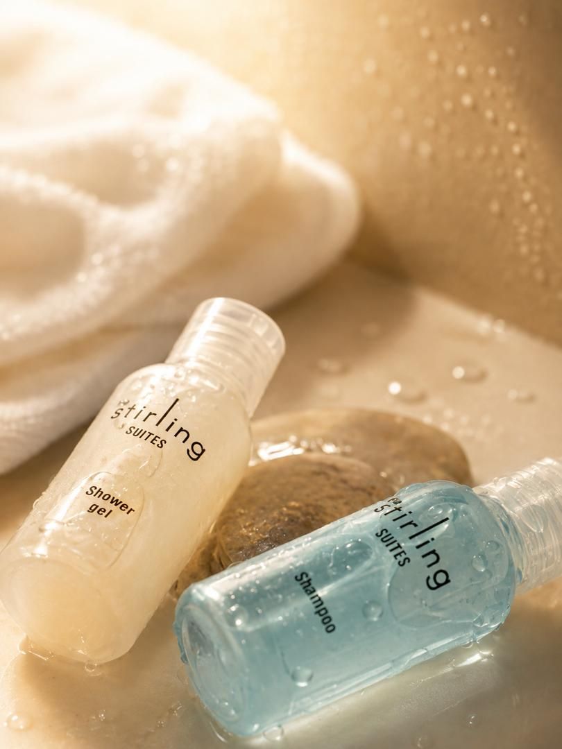 Dos ampolles de gel de dutxa i xampú de 'Stirling Suites' sobre una superfície amb gotes d'aigua.