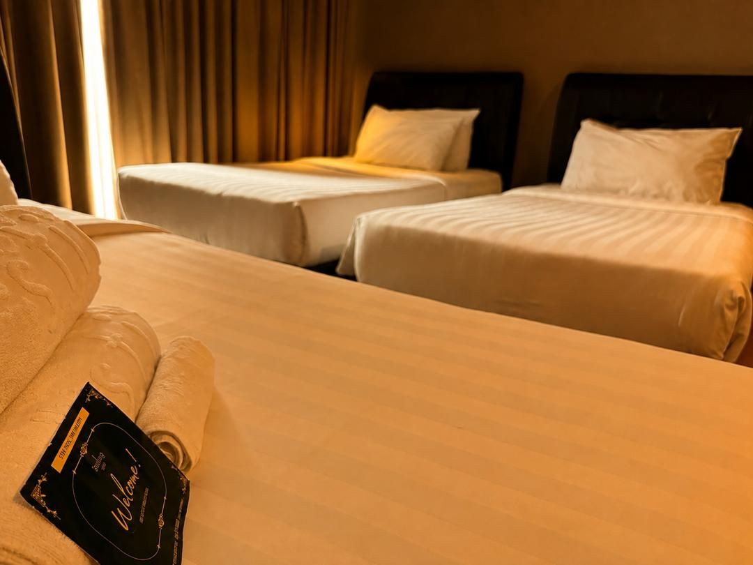 A hotel room with two single beds, a large bed, and a neatly made bed with a welcome card.