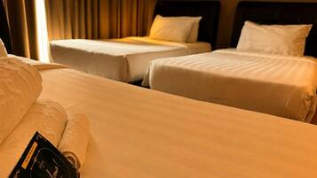 A hotel room with two single beds, a large bed, and a neatly made bed with a welcome card.