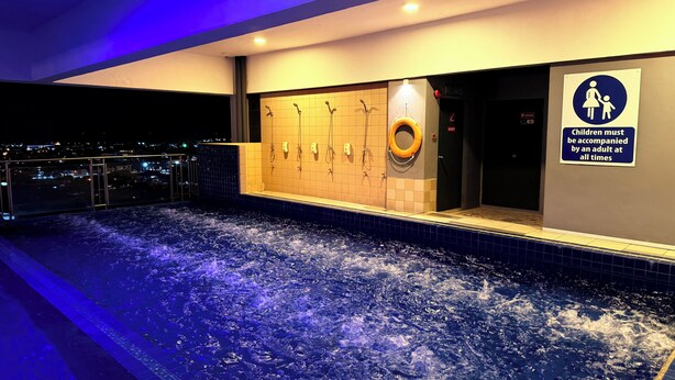 A heated indoor pool with multiple showerheads and a sign indicating children must be accompanied by an adult. - Stirling Suites (Miri)