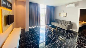 A hotel room with a black marble floor, a grey sofa, a flat-screen TV mounted on the wall, and a window with curtains. - Stirling Suites (Miri)