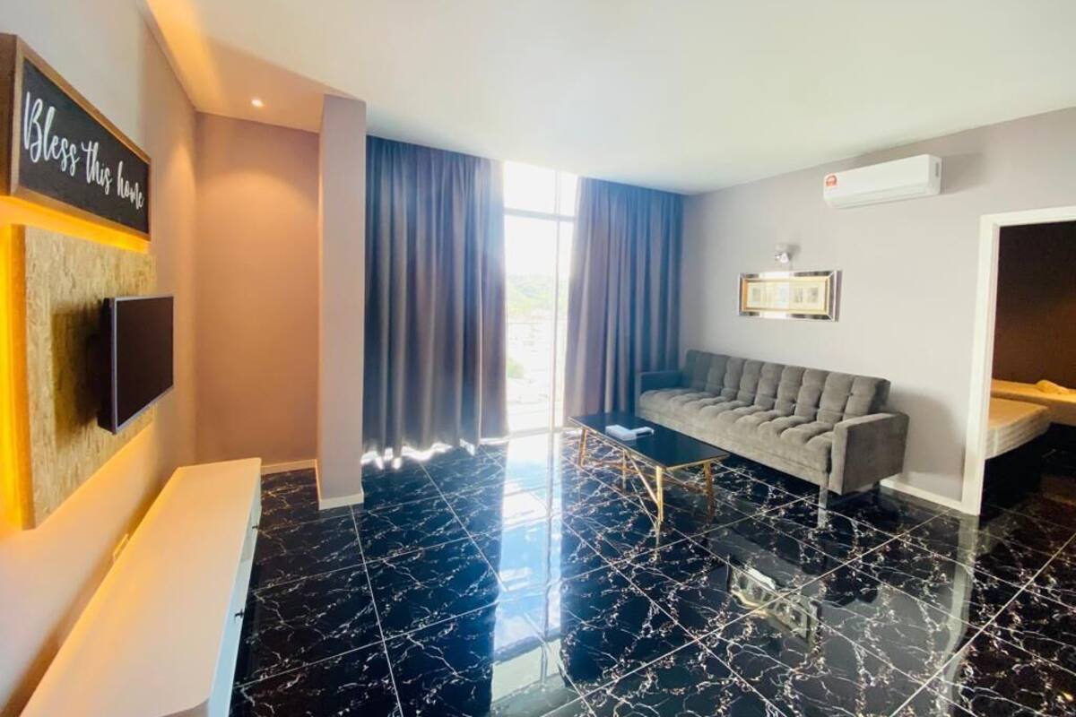 A hotel room with a black marble floor, a grey sofa, a flat-screen TV mounted on the wall, and a window with curtains.