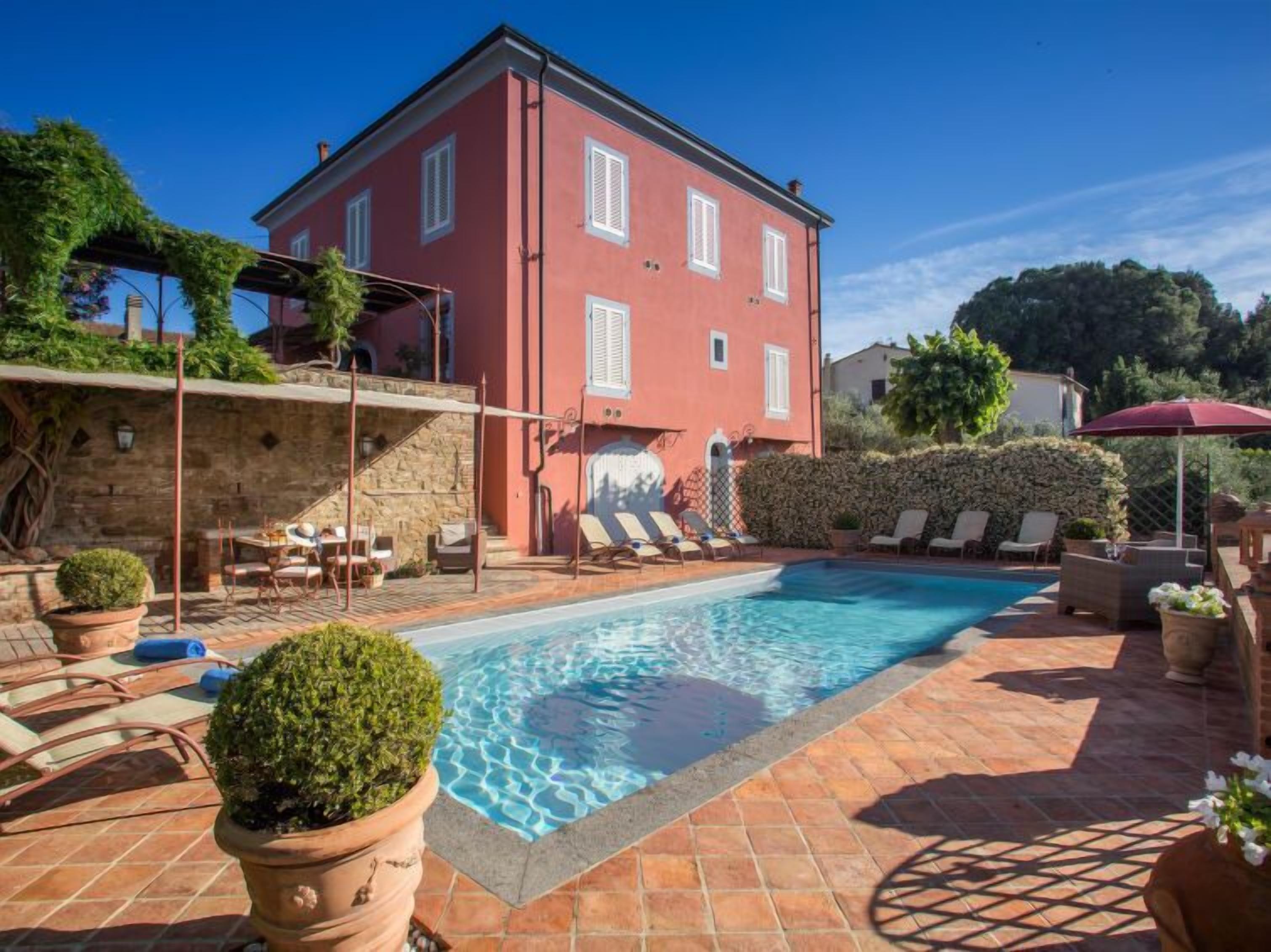 Eine rote Villa mit Swimmingpool, Sitzgelegenheiten im Freien und einer Steinmauer.