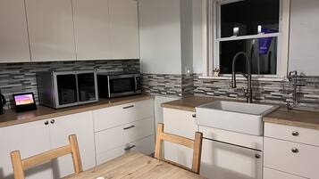 Une cuisine moderne avec des meubles blancs, deux micro-ondes encastrés, un plan de travail en bois, un évier et une fenêtre située au-dessus de l’évier.