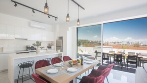 Eine moderne Küche mit weißen Schränken, ein Essbereich mit roten Stühlen und ein großes Fenster mit Blick auf die Stadt.