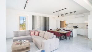 Ein modernes Wohnzimmer mit einer Eckcouch, einem Essbereich mit roten Stühlen und einer Küche mit weißen Schränken.