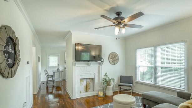 A living room with hardwood floors, a fireplace, a ceiling fan, and a large window with blinds. - 2 bedrooms, 1 bath, cozy kitchen, living room and game room/ multipurpose room. (Chattanooga)