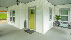 A covered porch with a yellow door, white siding, and a small bench with a potted plant. - 2 bedrooms, 1 bath, cozy kitchen, living room and game room/ multipurpose room. (Chattanooga)