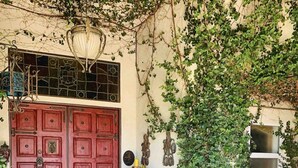 Puertas dobles rojas con un felpudo de cuadros, una pequeña mesa con adornos y una pared cubierta de hiedra.