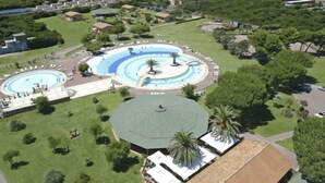 An aerial view of a resort with a central swimming pool, multiple guest villas, and a view of the ocean.