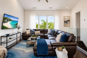 A modern living room with a sectional sofa, a coffee table, a TV, and a large window with curtains.
