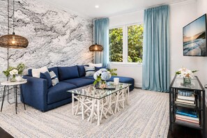 Un salon avec un canapé bleu, une table basse en verre et un mur orné d’un motif rappelant le marbre.