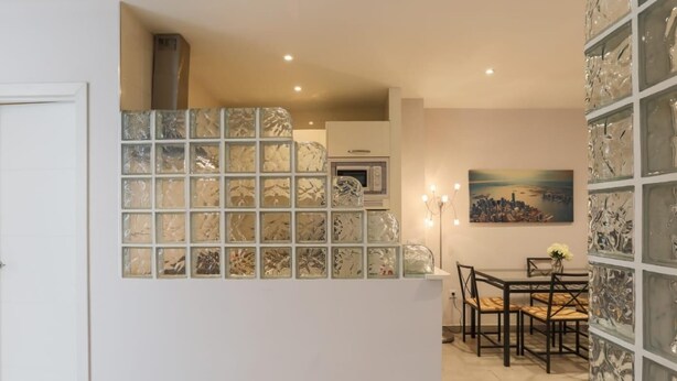 A modern kitchen with a central island, a dining area with a table and chairs, and a cityscape painting on the wall. - Green Street - Modern & quiet apartment in typical Sevilla house (Sevilla)