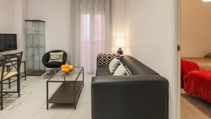 A modern living room with a black leather sofa, a glass coffee table with oranges, a glass cabinet, and a TV. - Green Street - Modern & quiet apartment in typical Sevilla house (Sevilla)