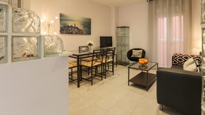 A modern living room with a dining area, featuring a glass coffee table, a black sofa, and a cityscape painting on the wall. - Green Street - Modern & quiet apartment in typical Sevilla house (Sevilla)