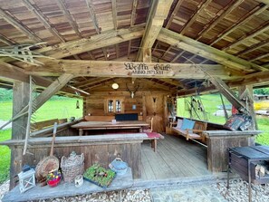 Une cabane rustique en bois, avec un plafond en bois, une grande table à manger au centre et une enseigne portant l’inscription « Bedra Gut Anno MMXII ».