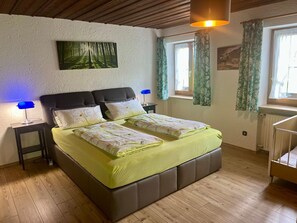 Une chambre à coucher avec un lit double, une table de chevet avec une lampe, une fenêtre avec des rideaux et un radiateur.