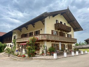 A two-story building with a balcony, outdoor seating, and a garden area.