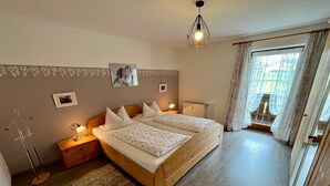 A bedroom with a double bed, bedside tables, a floor lamp, a rug, and a window with curtains.
