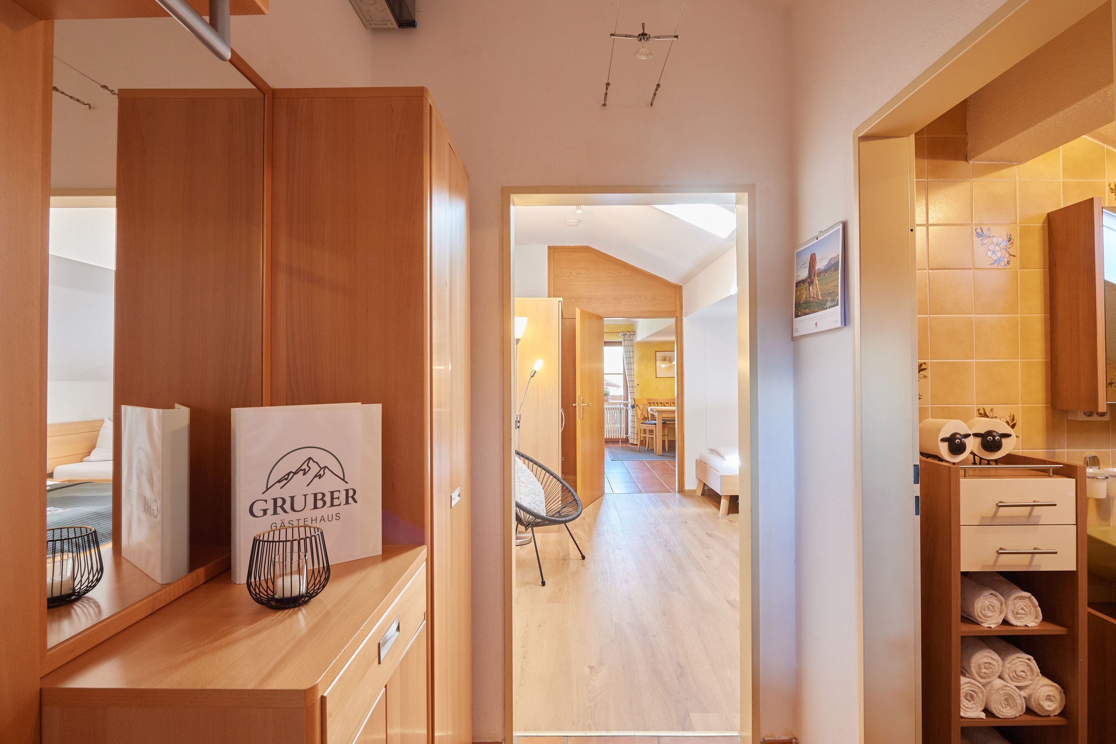 A hotel room with wooden furniture, a bed, a desk with a Gruber sign, and a bathroom with towels.