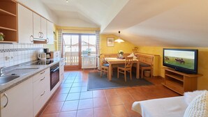 A compact kitchen with a dining area, a television, and a cozy seating space. - Type D Apartment Waginger See 2nd floor 50 sqm up to 3 persons, 1 bedroom, balcony (Piding)