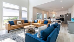 A spacious living room with a large sofa set, a coffee table, and a view of the kitchen and balcony. - LUXE Private Waterfront Retreat with Pool, Hot Tub and Game Room for Family Fun (Tracys Landing)