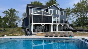 A two-story house with a large balcony, a swimming pool, and outdoor furniture. - LUXE Private Waterfront Retreat with Pool, Hot Tub and Game Room for Family Fun (Tracys Landing)