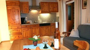 Une cuisine avec des meubles de rangement en bois, une table à manger avec une planche à découper, une bouteille et une chaise.
