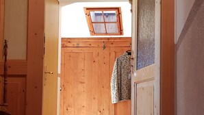 Un couloir intérieur en bois, avec une porte donnant sur une pièce, une petite fenêtre et un manteau accroché au mur.