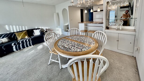 Une cuisine moderne avec des meubles blancs, un coin repas doté d’une table à motifs de mosaïque et un ventilateur de plafond.