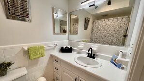 Une salle de bain avec un lavabo blanc, un miroir, un porte-serviettes, une poubelle et des toilettes.