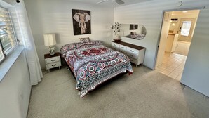 Une chambre à coucher comprenant un lit, une commode, un miroir, un ventilateur de plafond et une fenêtre.
