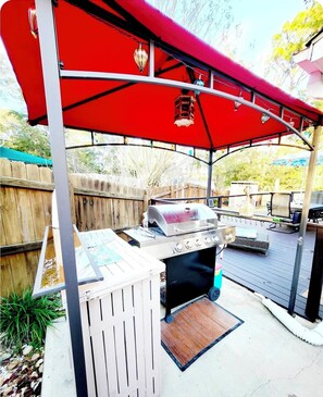 Een buitenbarbecue met een grill, een tafel en een rode luifel.