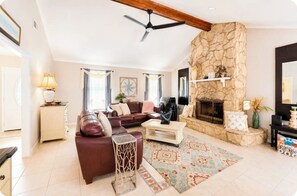 A living room with a stone fireplace, leather sofa, and a ceiling fan. - Coastal Retreat • Daphne • Near Fairhope • Hot Tub • Massage Chair• Gulf Beaches (Daphne)