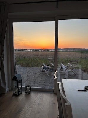 Quarto com uma grande janela com vista para o pôr do sol, duas cadeiras do lado de fora e uma mesa com uma caneta.