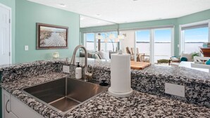 A kitchen with granite countertops, a stainless steel sink, and a large window overlooking a body of water. - Sauna Beach Haven 106 Direct Beach Access Near Downtown Tart Trail (Traverse City)